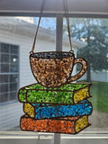 Hanging teacup and colorful stack of books suncatcher in a window